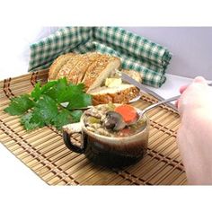 a person is holding a spoon over a bowl of soup with bread and parsley