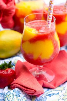 two glasses filled with liquid and strawberries next to lemons on a tablecloth