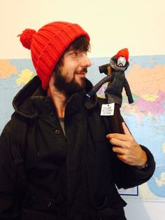 a man with a red knitted hat holding a small doll in front of a map