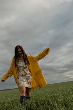 a woman in a yellow jacket is walking through the grass with her arms spread out