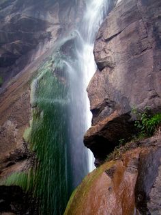 a large waterfall is coming out of the side of a rock face into the water