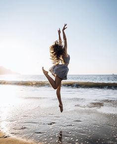 a woman jumping into the air on top of a sandy beach next to the ocean