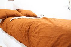 a bed with two orange pillows on top of it and a white wall behind it