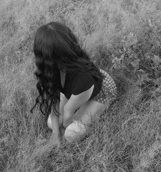 a woman kneeling down in the grass with her hands on her knees looking at something