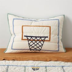 a pillow with a basketball hoop on it sitting on top of a bed next to pillows