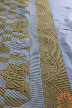 a close up of a quilt on a bed with an orange flower in the center