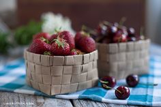 strawberries and cherries sit in baskets on a table