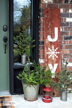 two potted plants sitting on the front porch next to a green door and red brick wall