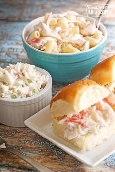 two plates with sandwiches and pasta salad in them on a blue tablecloth next to a bowl of macaroni salad