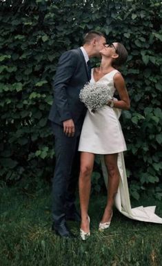 a bride and groom kissing in front of a hedge