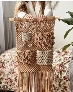 a woman is holding up a woven wall hanging with fringes and beadwork