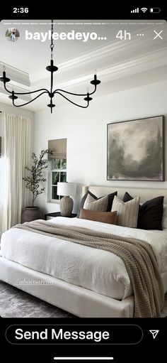 a white bed sitting under a chandelier in a bedroom next to a window