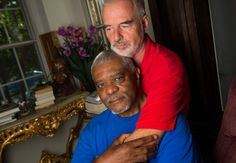 an older man is hugging the younger man's shoulder in front of a window