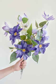 a bouquet of purple and white flowers being held by a woman's hand with long green leaves