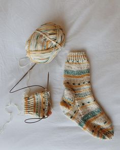 a pair of socks, yarn and knitting needles on a white sheet with a ball of thread