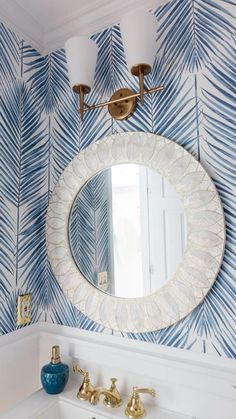 a bathroom with blue and white wallpaper, gold faucets and a round mirror