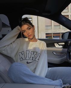 a woman sitting in the passenger seat of a car wearing a nike sweatshirt and jeans