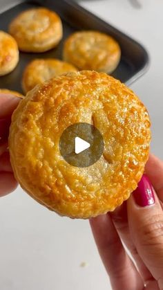 a person holding up a pastry in front of some muffins