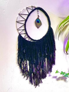 a purple and black dream catcher hanging from a wall next to a potted plant