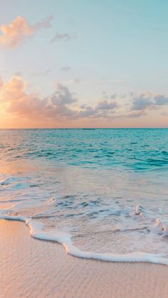 the sun is setting over the ocean with waves crashing onto the beach and sand on the shore