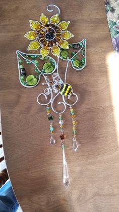 a wooden table topped with a glass sunflower and beaded necklace hanging from it's side