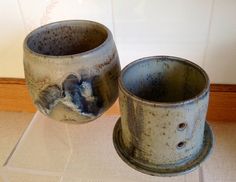 two gray cups sitting on top of a glass stand next to each other in front of a wall