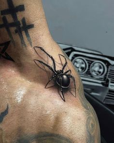 a black spider tattoo on the back of a man's arm and chest, with an inverted cross behind it