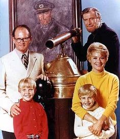 a group of people standing next to each other in front of a bell with a painting on the wall behind them