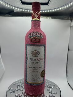 a bottle of pink wine sitting on top of a glass plate covered in jewels and beads