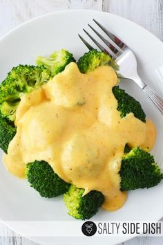 a white plate topped with broccoli covered in gravy next to a fork