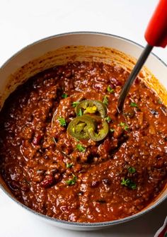 a pot full of chili with a spoon in it and a red pepper on the side