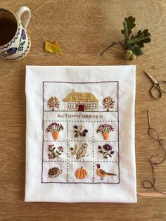 an autumn garden cross stitch pattern is displayed on a table next to a cup of coffee