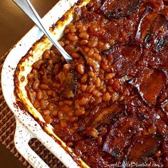 baked beans and onions in a casserole dish with two spoons on top