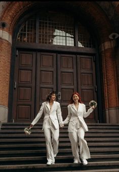 two women in white suits are walking down the stairs outside an old building holding hands