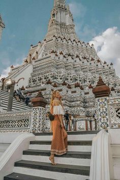 a woman standing in front of a white and gold building with stairs leading up to it