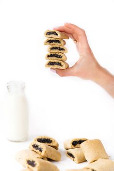 a hand is reaching for some cookies with blackberries on them next to a glass of milk