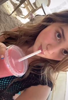 a young woman drinking from a pink cup with a straw in her mouth and looking at the camera