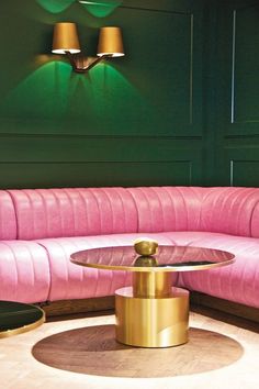 a pink couch sitting in front of a green wall with two lamps on top of it