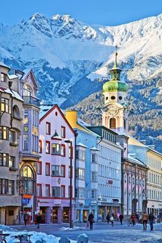 people walking on the street in front of buildings with mountains in the backgroud