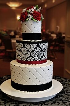 a three tiered cake with black and white designs on the bottom, red flowers on top