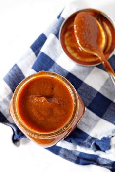 two jars filled with sauce sitting on top of a blue and white checkered cloth