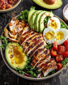 a salad with chicken, avocado, tomatoes and sliced eggs on the side