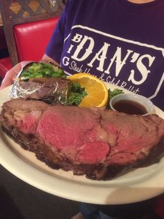 a person holding a plate with steak, broccoli and orange slices on it