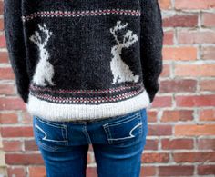 the back of a woman's sweater with reindeers on it in front of a brick wall