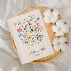 an open book sitting on top of a wooden plate next to some cotton balls and flowers