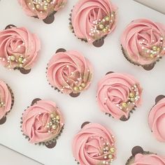 cupcakes with pink frosting and gold decorations are arranged on a white tray