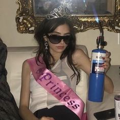 a woman sitting on top of a couch holding a blue water bottle and wearing sunglasses