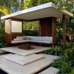 an outdoor living area with white furniture and trees in the background, surrounded by greenery