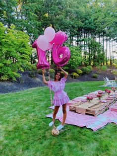 a woman holding up pink balloons in front of a picnic table with food and drinks on it