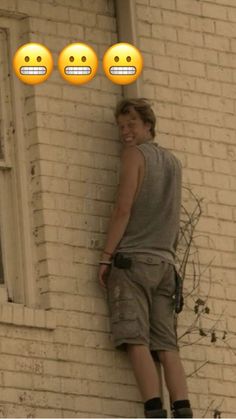 a young man standing next to a brick building with emoticions on the wall